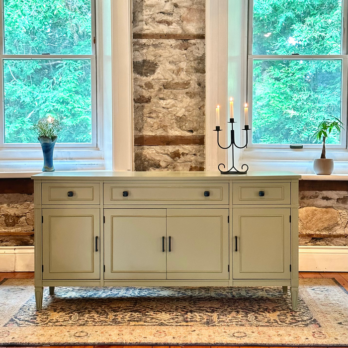 Light green sideboard against a stone wall with two windows