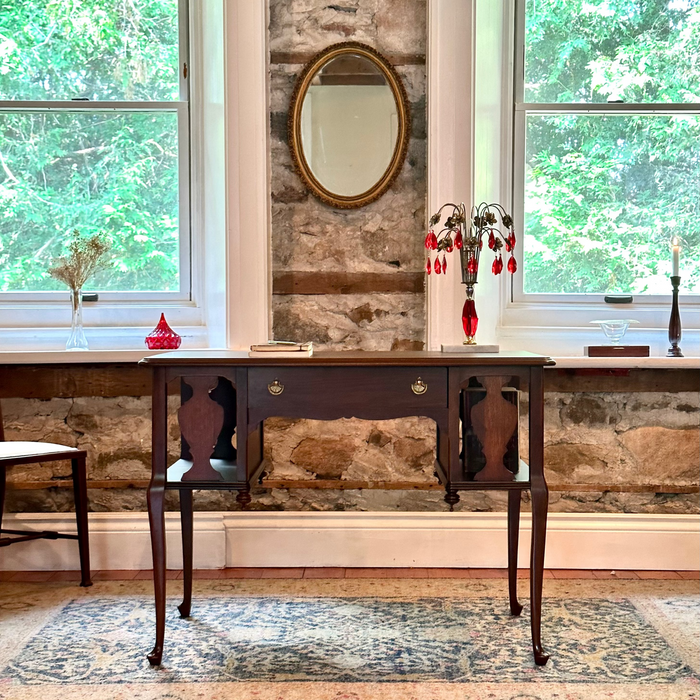 Wooden desk with decorative items against a stone wall with large windows.