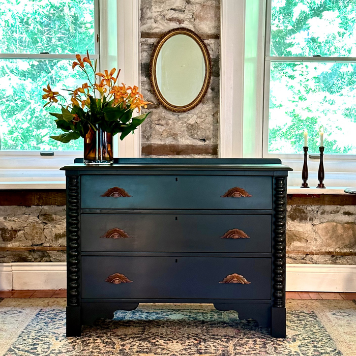 Black panther dresser with floral arrangement in a room with stone wall and windows.