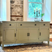 Green sideboard with candle holder and plant in a room with stone wall and window.