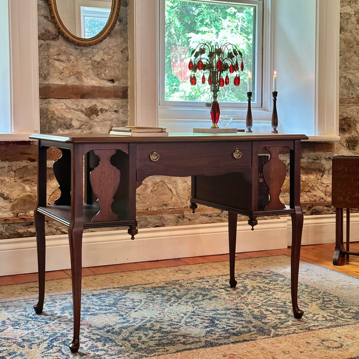 Wooden desk in a room with stone walls and a large window.