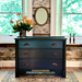 Black panther dresser with floral arrangement in a room with stone wall and windows.