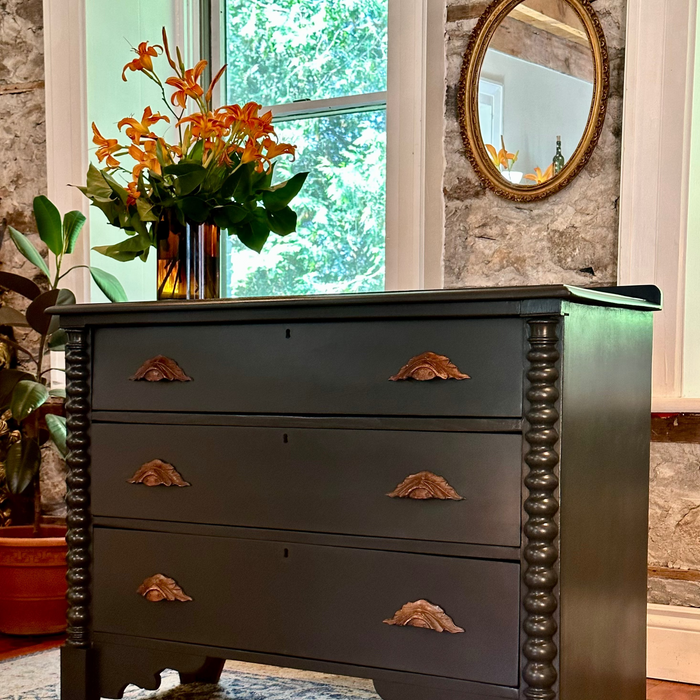 Dark wooden dresser with wood moustache handles in a room with a window and mirror.