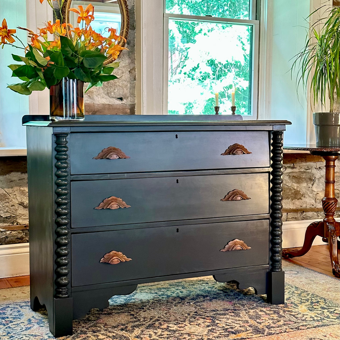 Black panther dresser with wood handles in a room with a window and decorative mirror.