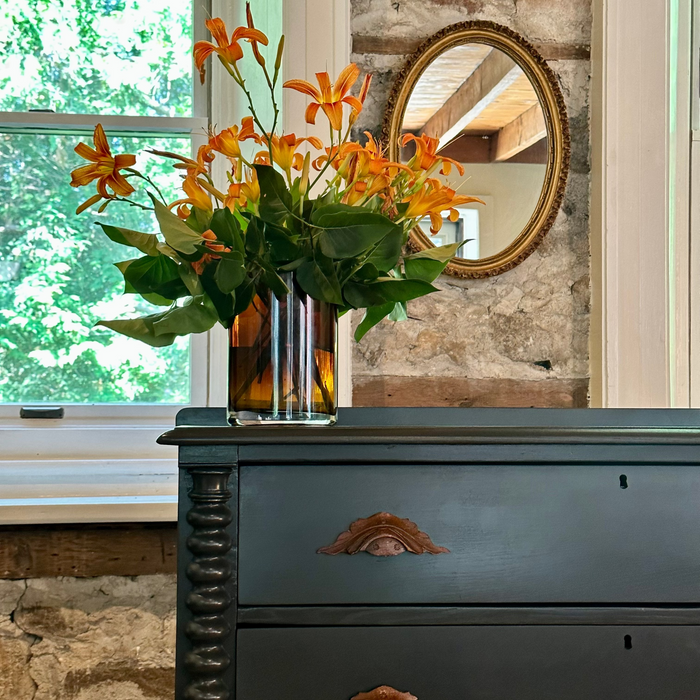 Decorative vase with orange flowers on a dark wooden dresser against a stone wall.